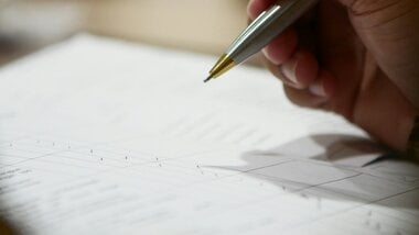 A hand holding a pen over a sheet of paper with a graph or chart.